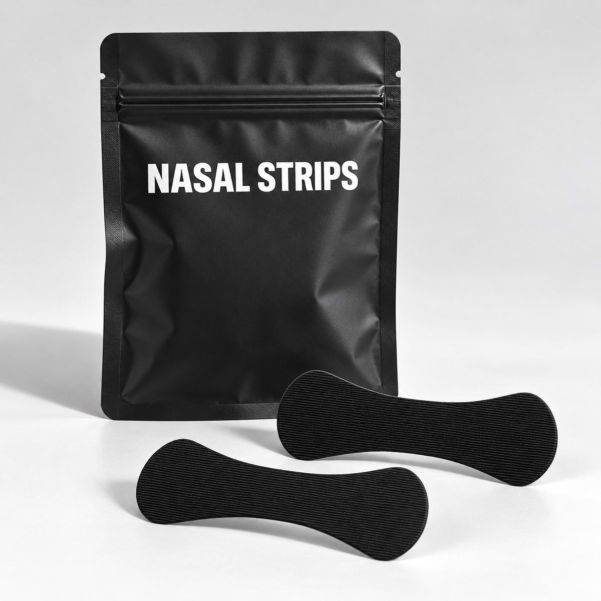 Black nasal strips and matte black pouch on a gray studio surface
